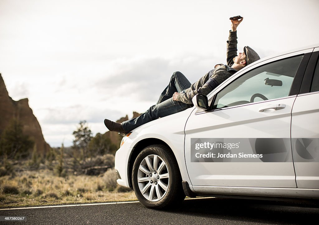Man laying on his car using his cell phone.