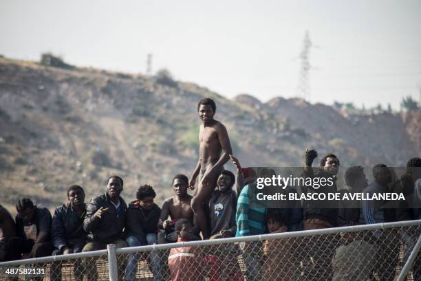 Would-be immigrants, one of them naked, sit atop a boarder fence separating Morocco from the north African Spanish enclave of Melilla on May 1...