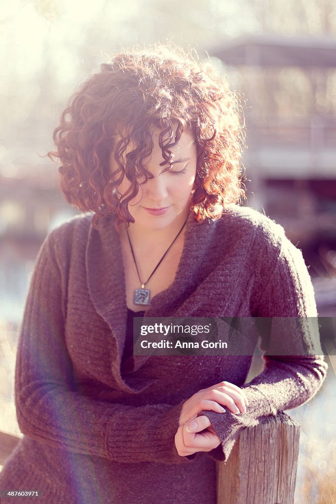 Young woman rests hand on fencepost, looking down