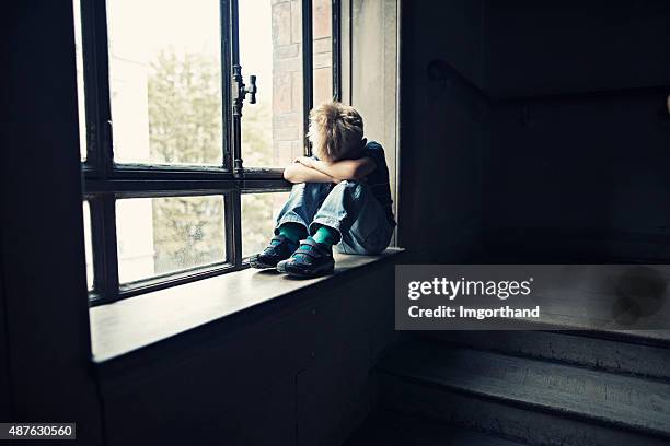 depressed little boy in old staircase - childhood poverty stock pictures, royalty-free photos & images