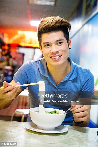 young vietnamese man demonstrating how to eat pho with chopsticks - vermicelli stock pictures, royalty-free photos & images