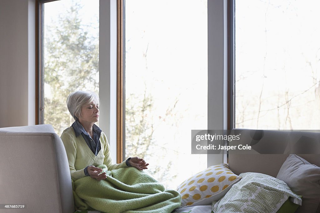 Senior woman meditating on sofa