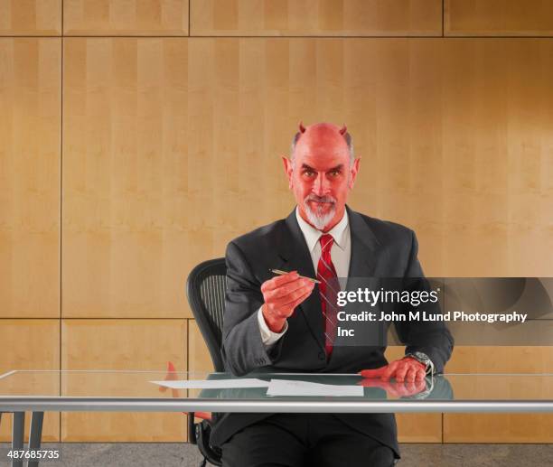 caucasian businessman in devil costume offering pen to sign contract - devil stock-fotos und bilder