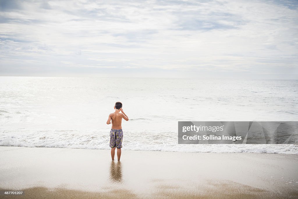 Hispanic boy standing in surf at beach