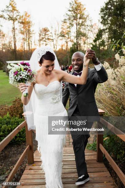 newlywed couple walking on wooden footbridge - front on groom and bride stock pictures, royalty-free photos & images