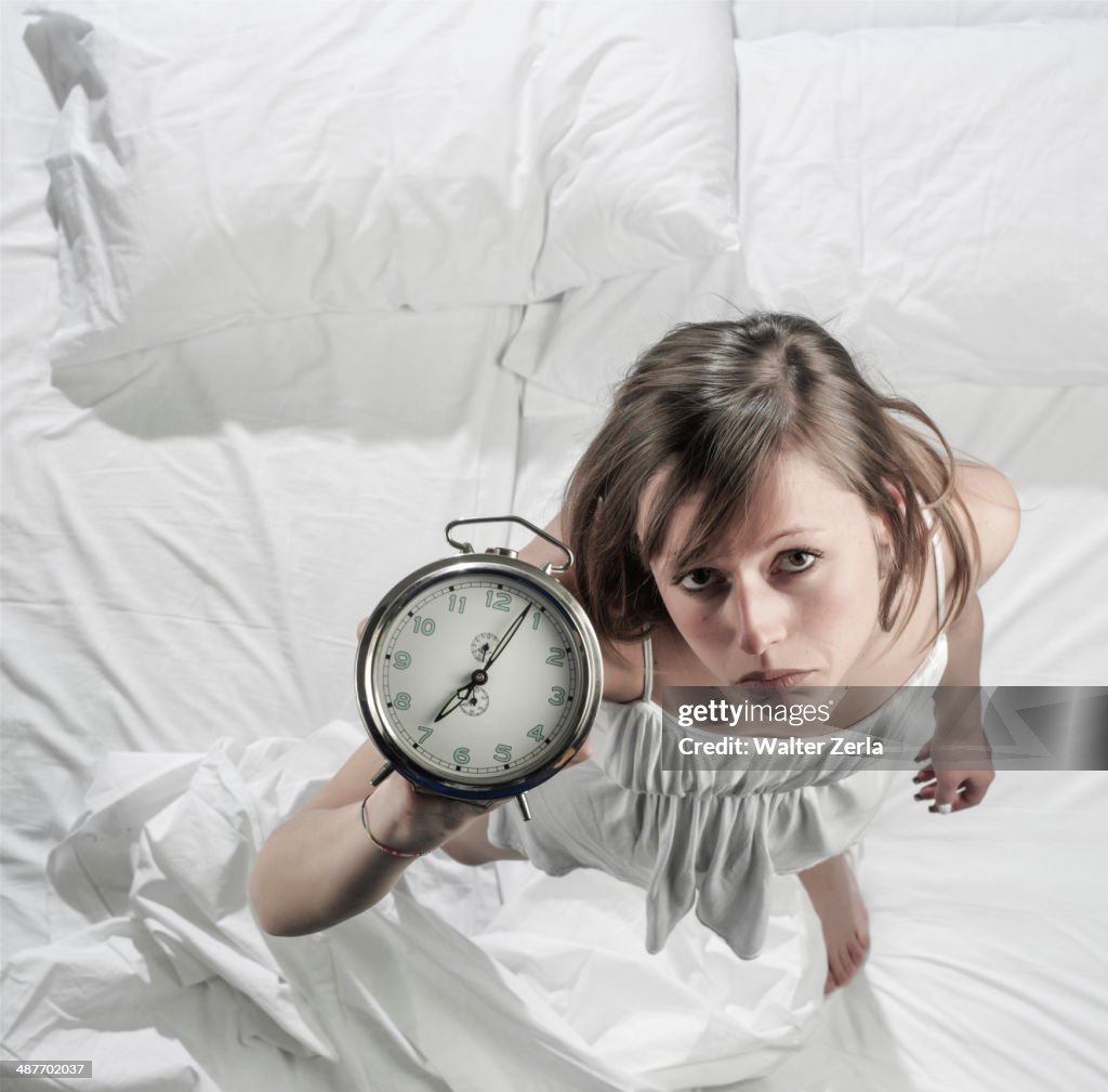 Hispanic woman holding alarm clock in bed