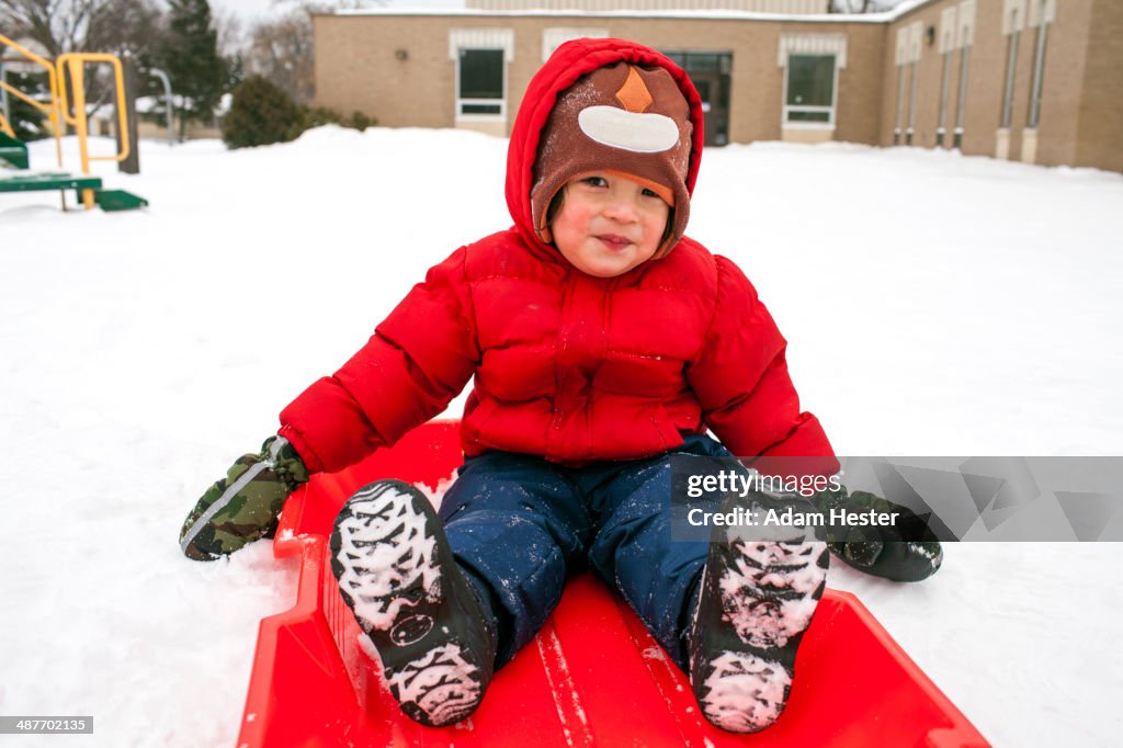 Mixed race boy sitting on sled in snow