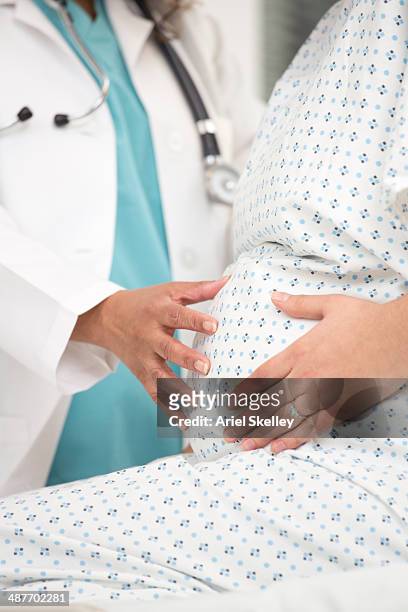 mixed race doctor examining pregnant patient's belly - prenatal care stock pictures, royalty-free photos & images