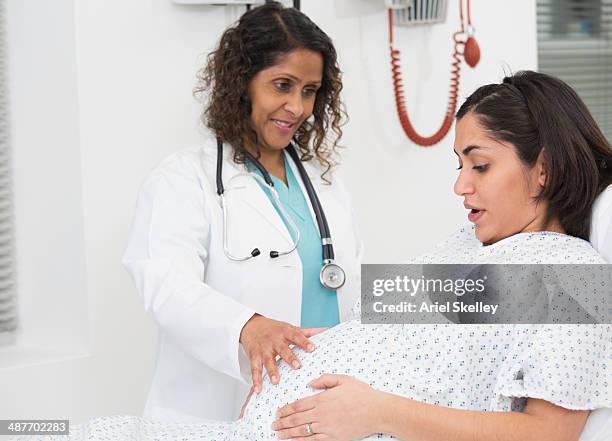 mixed race doctor examining pregnant patient's belly - pregnant woman at doctor stock-fotos und bilder
