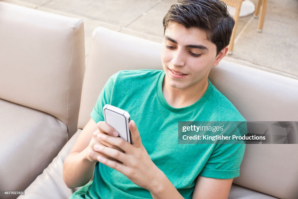 Mixed race teenage boy using cell phone on sofa