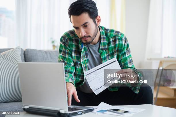 mixed race man paying bills in living room - home finances man stock pictures, royalty-free photos & images