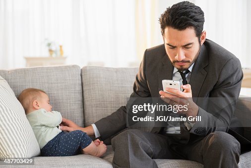 Father sitting with baby and using cell phone Father sitting with baby and using cell phone