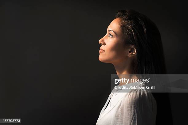 hispanic woman looking up into light - black background portrait stockfoto's en -beelden