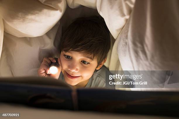hispanic boy reading under covers - six under ストックフォトと画像