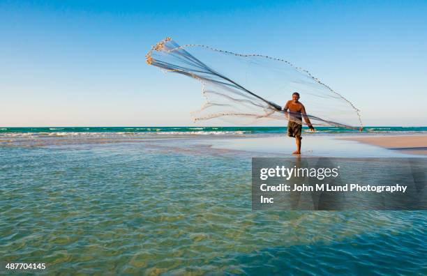 middle eastern fisherman casting net on tropical beach - commercial fishing net stock-fotos und bilder