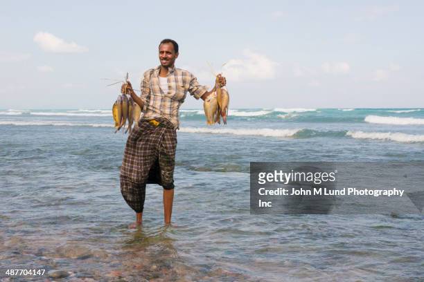 middle eastern fisherman holding catch on beach - yemen people stock pictures, royalty-free photos & images