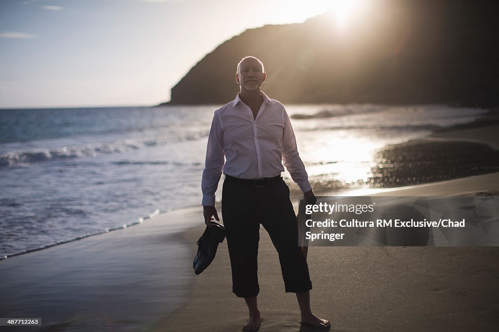 Portrait of retired businessman at coast, holding shoes and tie