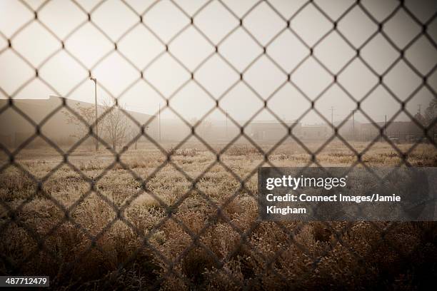 Industrial Structures And Abandoned Land Behind Metal Fence, Foto de stock