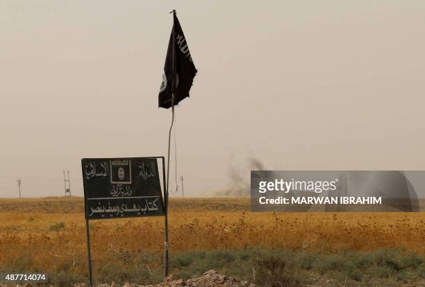 Smoke rises in the distance behind an Islamic State group flag and banner after Iraqi Kurdish Peshmerga fighters reportedly captured several villages...