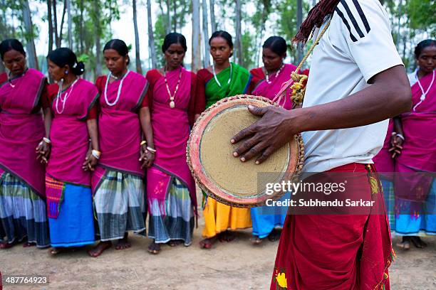 Santhali man plays a drum as women prepare to dance. The Santhal are the largest tribal community in India. They have a distinct culture of their...