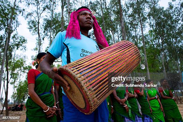 Santhali man plays a drum while women wait to begin dancing in the background. The Santhal are the largest tribal community in India. They have a...