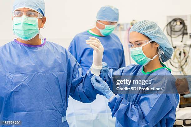 surgical nurse assisting surgeon with gloves and gown in or - operatiegewaad stockfoto's en -beelden