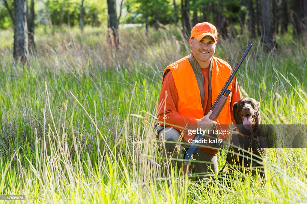 Man hunting with shotgun kneeling next to retriever