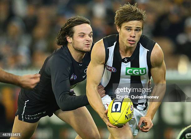 Josh Thomas of the Magpies handballs whilst being tackled by Dylan Buckley of the Blues during the round seven AFL match between the Carlton Blues...