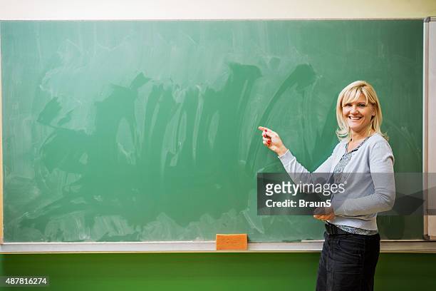 smiling female teacher pointing at blackboard. copy space. - teacher board stock pictures, royalty-free photos & images