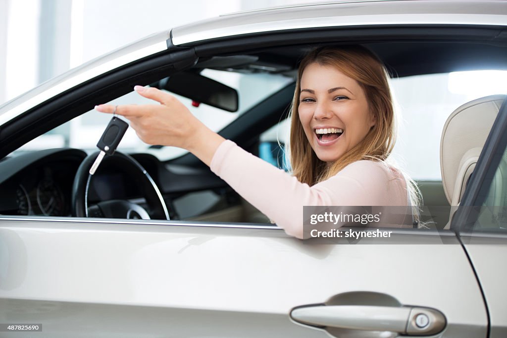 Cheerful woman sitting in a car holding new car keys.