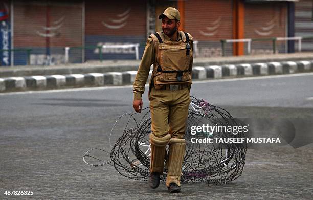 An Indian policeman pulls a barbed wire fence during a curfew in the Maisuma locality of Srinagar on May 2, 2014. Parts of Kashmir remained under...