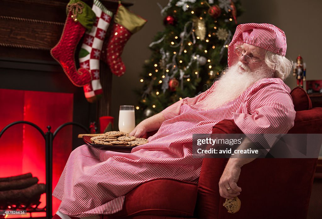 Cansado Santa dormindo com leite e biscoitos com lareira