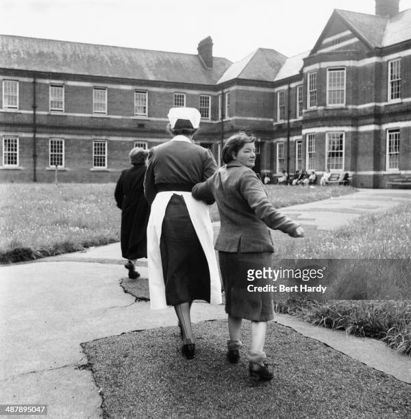 Female patient is led away by a nurse after spending time in the grounds at at the Netherne Mental Hospital near Coulsdon, Surrey, 1953. Original...