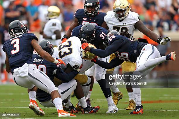 Running back Josh Adams of the Notre Dame Fighting Irish is tackled by cornerback Maurice Canady of the Virginia Cavaliers and teammates in the first...