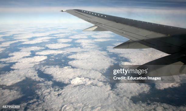 Airplane wing of plane cruising in blue sky high above clouds over Europe.