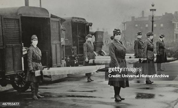 St. Louis Red Cross Motor Corps on duty during the American Influenza epidemic. 1918. Mask-wearing women holding stretchers at backs of ambulances.