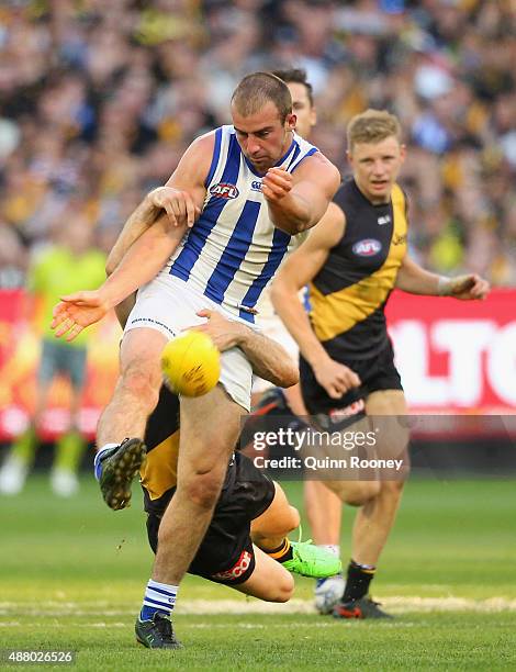 Ben Cunnington of the Kangaroos kicks whilst being tackled by Trent Cotchin of the Tigers during the First AFL Elimination Final match between the...