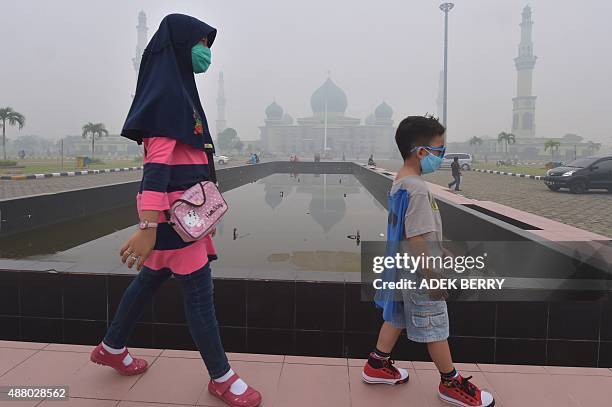 Woman and young boy walk past the An-Nur Great Mosque as haze shrouds the Sumatran city of Pekanbaru, in Riau province on September 13, 2015. Smog...