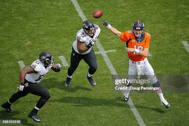 Quarterback Peyton Manning of the Denver Broncos passes under pressure by outside linebacker Terrell Suggs and defensive end Lawrence Guy of the...