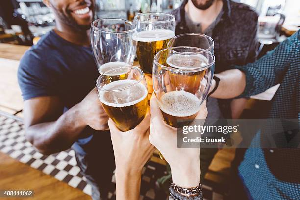 friends toasting with beer in a pub - hand-holding-pint stock pictures, royalty-free photos & images