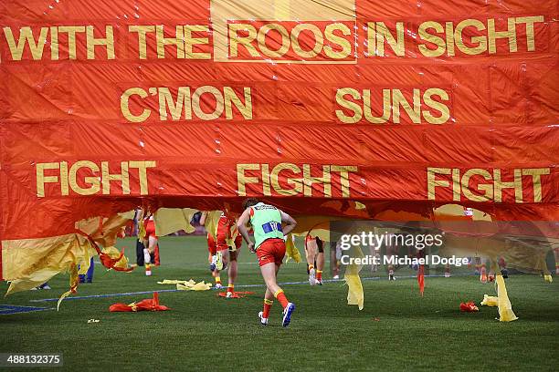 Suns players run through their banner during the round seven AFL match between the North Melbourne Kangaroos and the Gold Coast Suns at Etihad...