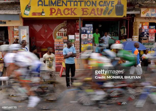 Bystanders look on as the pack of Cyclists competing in 150km cycling final in the the 11th Africa Games ride through an urban area on September 13,...