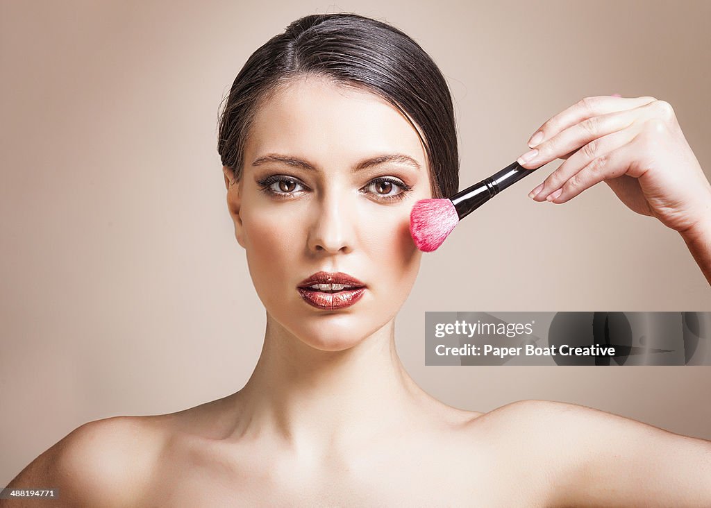 Woman applying blush on to her cheeks