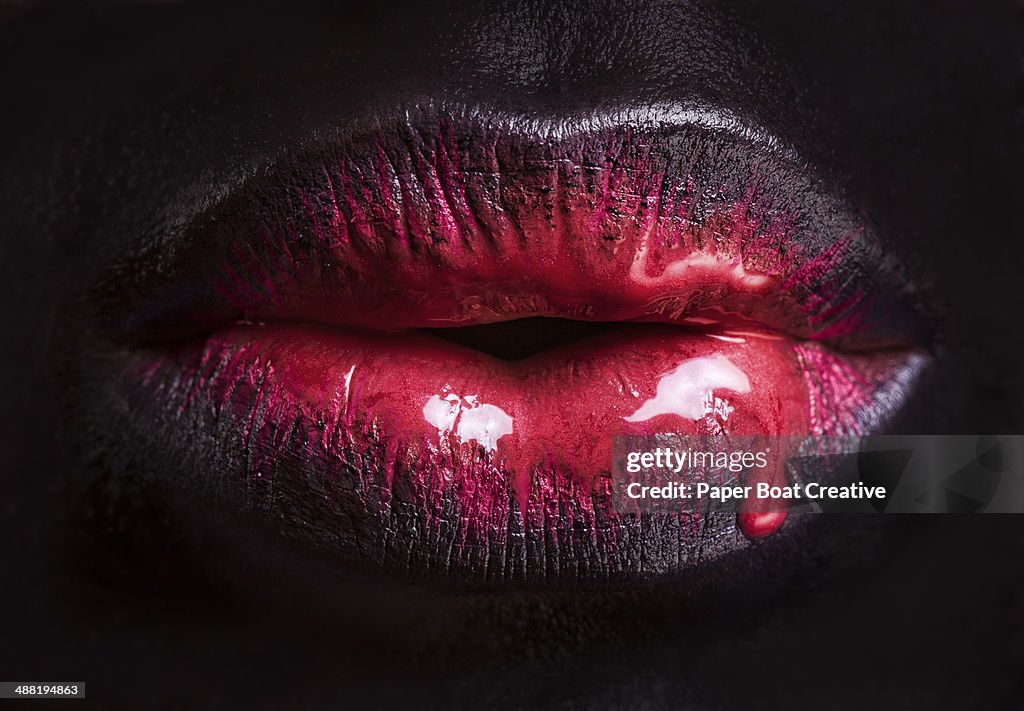 Close up of red paint dripping over black lips