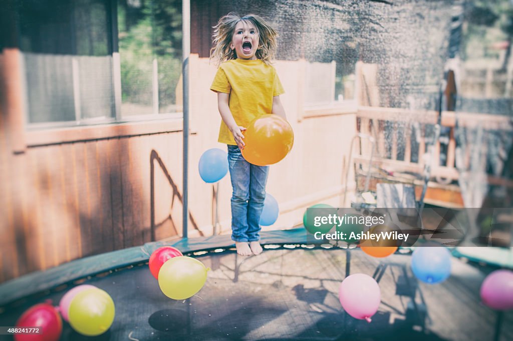 Child jumps on trampoline laughing with balloons