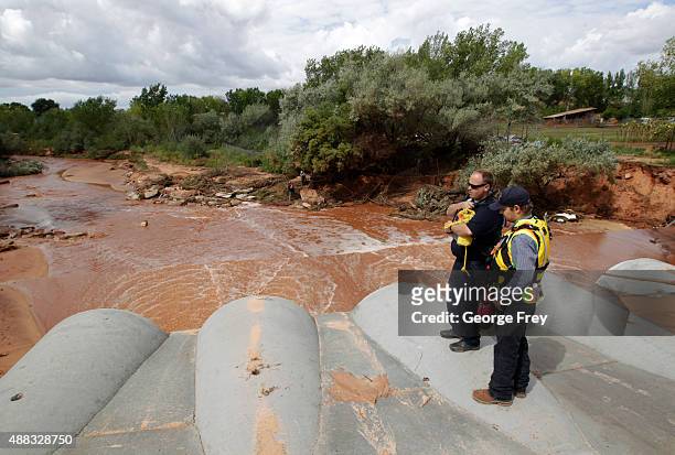 Two rescue personnel stand watch on pipes as other rescuers search Short Creek where two vans were swept away the day before on September 15, 2015 in...