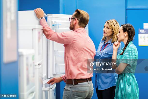young couple buying refrigerator in appliance store - appliance shopping stock pictures, royalty-free photos & images