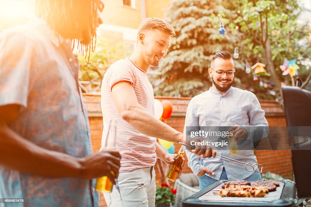 Young Men Grilling Meat At Barbecue Party.