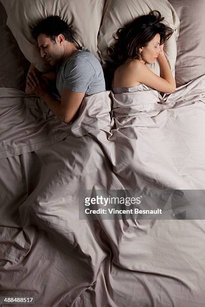 woman and a man lying back to back in  bed - doing the splits stockfoto's en -beelden