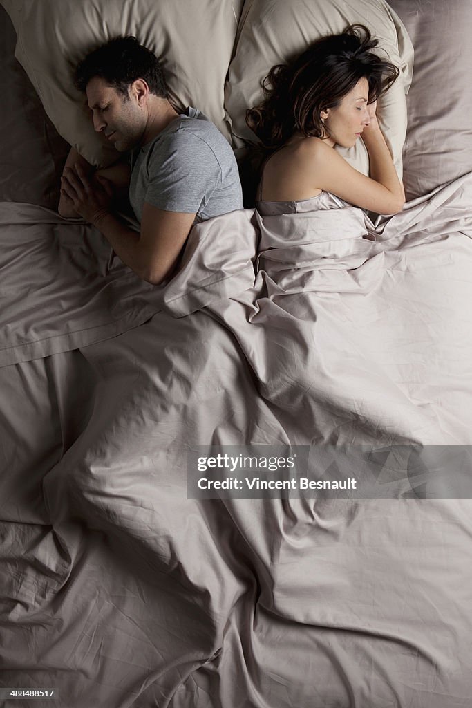 Woman and a man lying back to back in bed